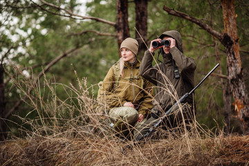 männlicher Jäger mit Fernglas, der bereit ist zu jagen, Waffe zu halten und im Wald spazieren zu gehen.