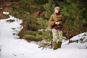 Female hunter in camouflage clothes ready to hunt, holding gun and walking in forest.