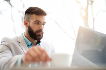 Side view of man in suit checking emails on laptop drinking coffee.