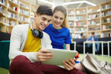 Portrait of smiling students couple, boy and girl, using digital tablet looking at screen in lounge...