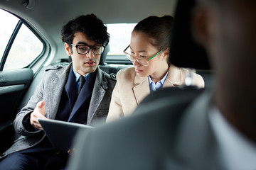 Portrait of two successful business people riding on backseat of car: man and woman discussing work documents in taxi