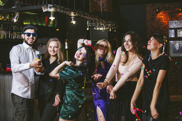 Young cheerful company of friends in the club bar having fun with multi-colored confetti and crackers celebrate