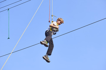 Cute school boy enjoying a sunny day in a climbing adventure activity park. Clear blue sky background. Children summer activities.