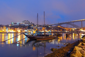 Fototapeta premium Traditional rabelo boats with barrels of Port wine on the Douro river, Ribeira and Dom Luis I or Luiz I iron bridge on the background, Porto, Portugal.