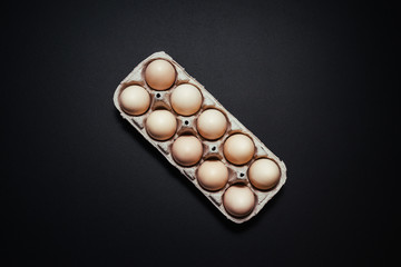 Cardboard egg box on black wooden background. Top view with copy space. Eggs container.
