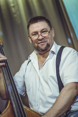A European male 35-45, middle-aged, plays a restaurant on a contrabass on stage.