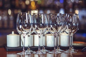 Wine glasses stand on the bar. The multicolored bar shelf is defocused.