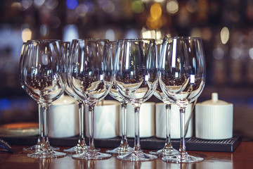 Wine glasses stand on the bar. The multicolored bar shelf is defocused.