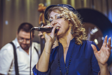 Fototapeta premium Vocal group in the restaurant. A European woman sings, a man unfocused playing the double bass.