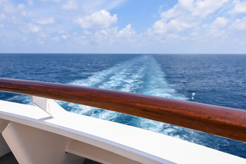 Fototapeta na wymiar Backside of a cruise ship, with trail in the blue ocean.