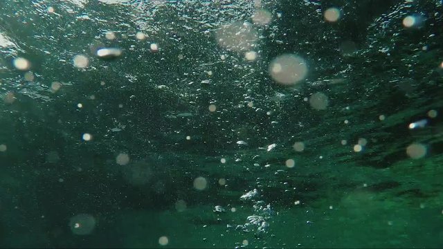 Diver emerges to the surface in the frame, hands are visible with a compensator button to control the ascent rate. Around a lot of air bubbles