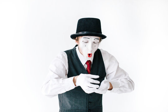 Funny mime in black hat looks at something invisible in his arms