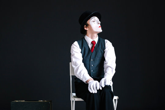 Attache case stands before mime while he sits on the chair