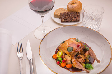 Table layout by the stuffed quail with sauce from a lavender, root crops and red currant with a glass of red wine and a basket of home-made bread