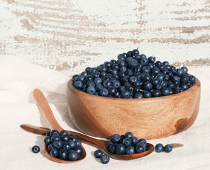 Fresh blueberries in a wooden round plate with a wooden spoons