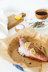 Cooking and marinating sea fish at home. Red perch with lemon, pepper and rosemary lies on parchment paper.