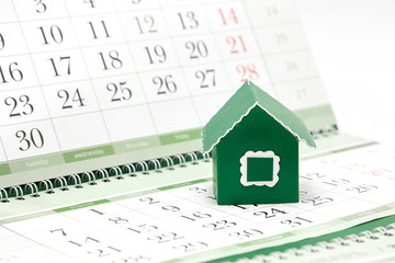 Cardboard green house on the background of the calendar / Russian translation: Monday, Tuesday, Wednesday, Thursday