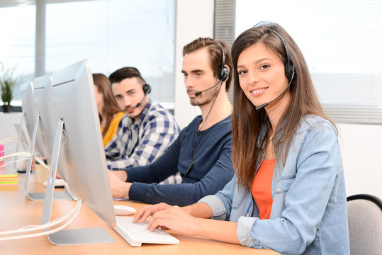 portrait of beautiful and cheerful young woman telephone operator with headset working on desktop computer in row in customer service call support helpline business center