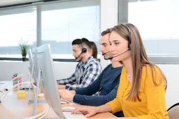 portrait of beautiful and cheerful young woman telephone operator with headset working on desktop...