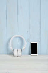 Cascos o auriculares y teléfono en mesa de madera blanca y pared azul