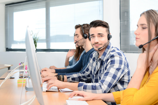 portrait of handsome young man telephone operator with headset working on a desktop computer in row in customer service call support helpline business center