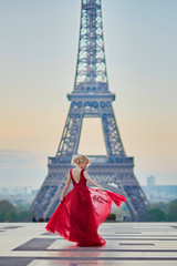 Woman in long red dress dancing near the Eiffel tower in Paris, France