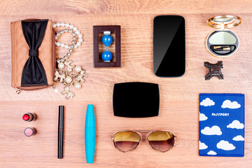 Top view. Objects of a traveller isolated on wooden background: smartphone, passport, sunglasses, wallet, necklace,eyeliner, lipsticks and mascara, eyeshadow, mirror and souvenirs
