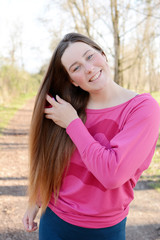 Fototapeta premium The portrait of beautiful young woman brushing her hair in the park.