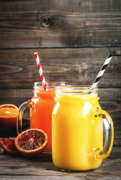 Refreshing summer drink. Juice from classic oranges and red Sicilian oranges. On a rustic wooden table, with whole and cut oranges. Copy space