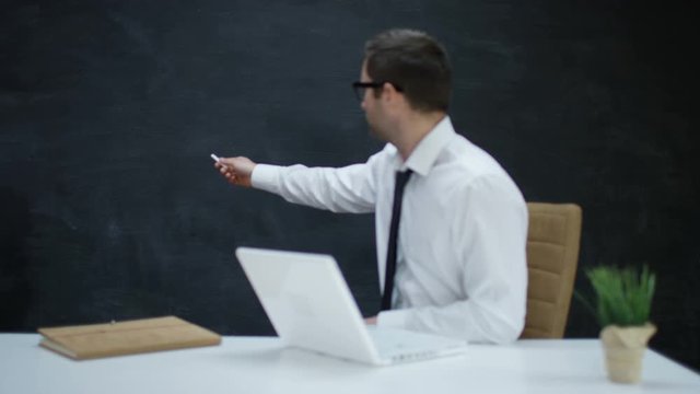 Businessman with laptop moving his hand as if underlining a word on chalkboard
