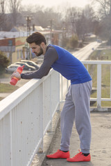 Jogger with bottle of water leaning on fence