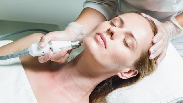 Professional beautician massaging female face by device