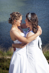 Fototapeta na wymiar just married happy lesbian couple in white dress near small lake look each other in the eyes