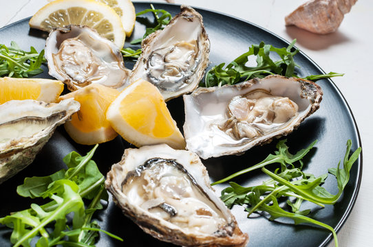 Oysters with lemon fruit on a black plate on a white wood table.