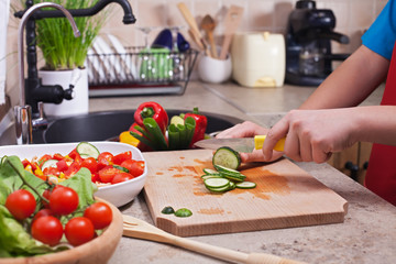 Child hands chopping vegetables on cutting board - slicing the cucumber