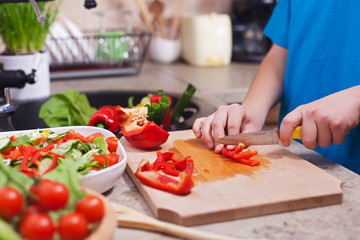 Child hands chopping vegetables on cutting board - the red bellpepper