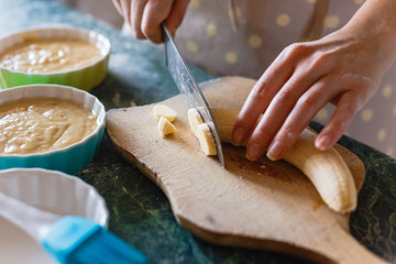 Woman cuts a banana with a knife on rude wooden board