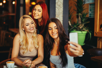 Three beautiful young woman doing selfie in cafe