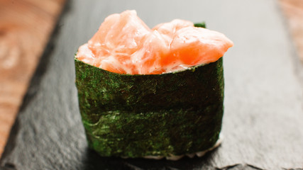 Appetizing piece of delicious and fresh sushi served on black slate. One Japanese maki roll, close up. Traditional cuisine. © Photodrive