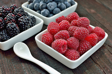 Mix of blueberries, blackberries and raspberries fruit on wood table. Forest fruit in white idaeus with spoon. Delicious fresh berries.