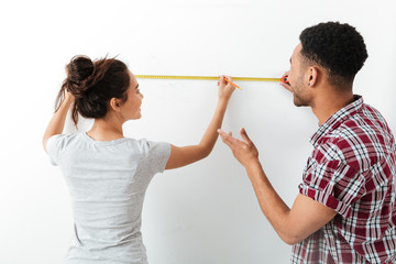 Happy young couple standing and using measuring tape