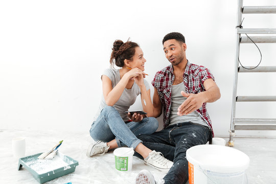 Happy multiethnic young couple renovating home and using mobile phone