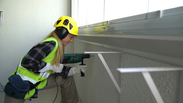 Young Female construction worker drilling concrete wall with the drill and smiling at the camera.