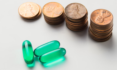 3 green capsule drugs on white background with soft focus stack of 1 Cent coin in glass jar