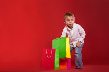 Little boy peers into packages with gifts on a red background