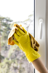 Window cleaning. Female hands in yellow gloves. With a bullet and a yellow rag