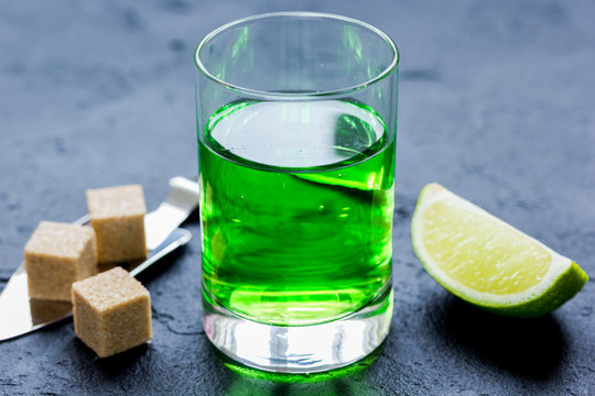 absinthe with sugar cubes in spoon on dark background