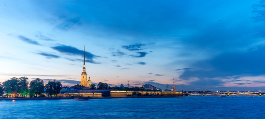 Peter and Paul fortress with the Palace promenade at sunset on a background of pure pink sky with reflection in the water of the Neva river during the white nights in St. Petersburg