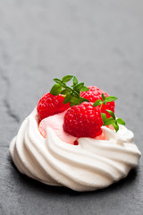 Mini  Pavlova meringue nest with raspberries and thyme on black stone background