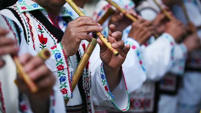 People in romanian traditional costumes singing at wooden flutes